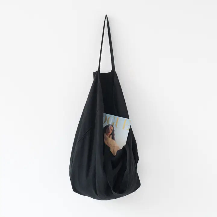 Musta Black Linen Big Bag pellavainen kangaskassi jossa on Voguen lehti sisällä ja kassi roikkuu seinällä.