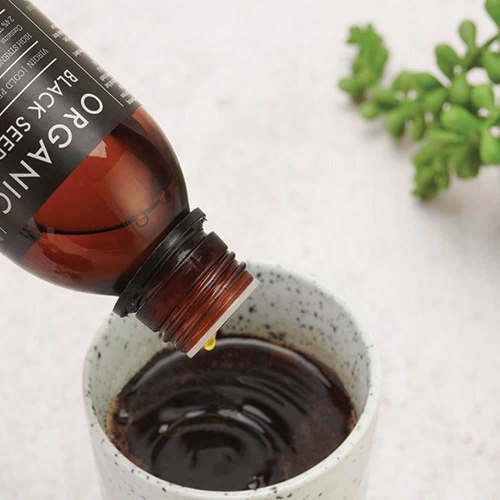 Kiki Healthin Black seed oil tippoja tiputetaan kahvikupillisen joukkoon, kuvituskuva.